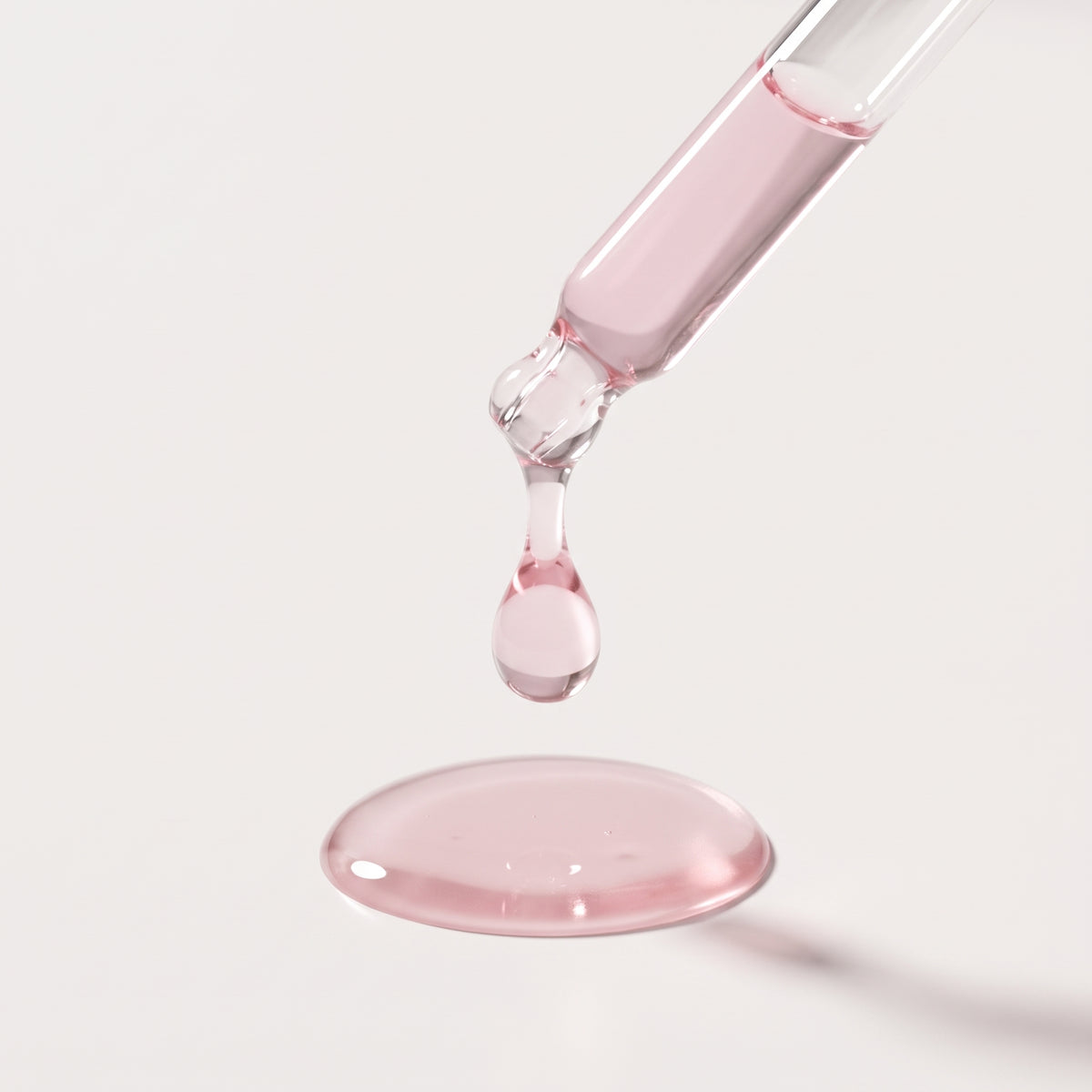 Close-up of a dropper releasing a drop of Lumi PDRN Pink Peptide Glow Serum onto a white surface