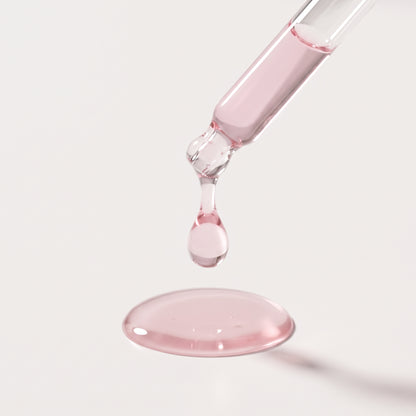 Close-up of a dropper releasing a drop of Lumi PDRN Pink Peptide Glow Serum onto a white surface