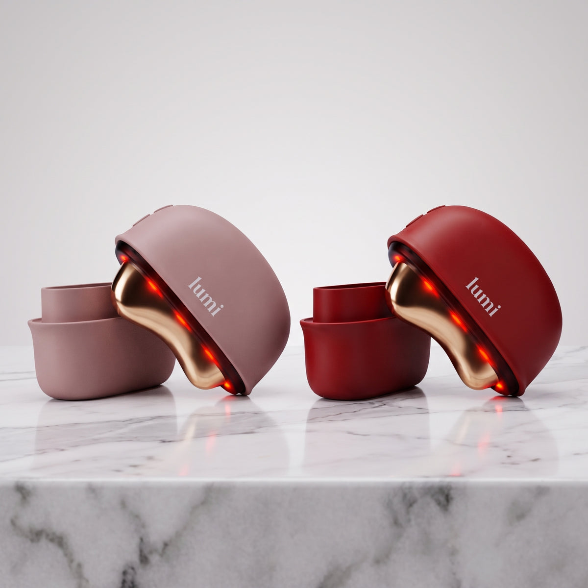 Lumi Ember heated gua sha in rosé and ruby colours side by side on white marble